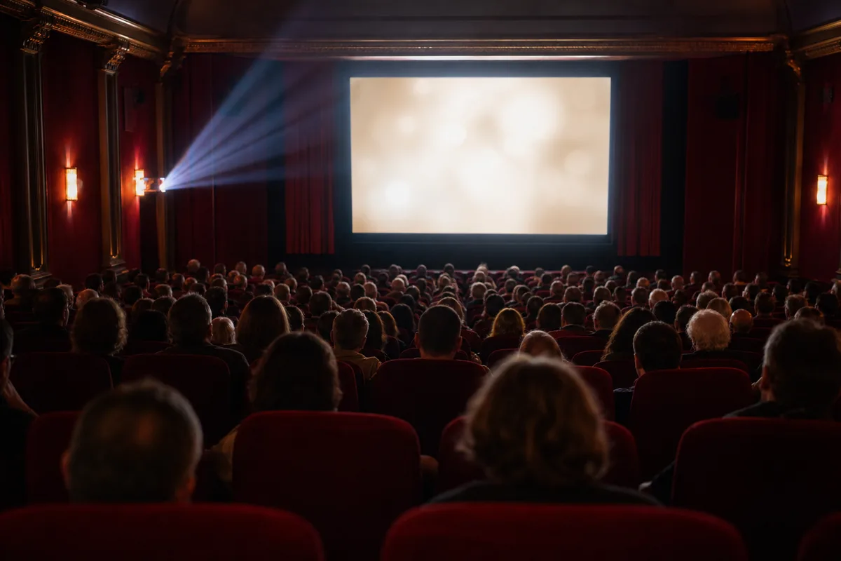 Salle de cinéma comble vue de dos, spectateurs face à un écran lumineux